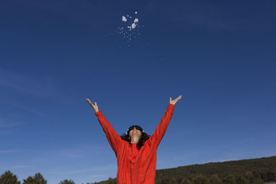 Cheerful woman throwing snow against sky