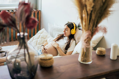 Pregnant young woman lies resting on the bed with headphones listening to music for pleasure. 