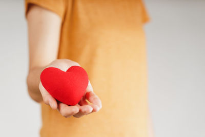 Midsection of woman holding heart shape over white background