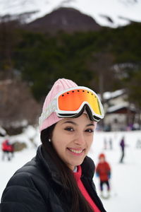 Portrait of smiling woman in ski goggles against mountains
