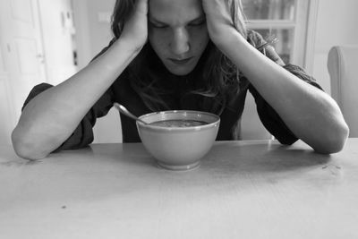 Depressed young woman sitting by soup at table
