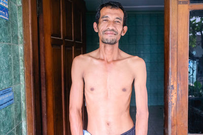 Portrait of shirtless man standing against door