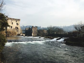 Buildings by river against sky