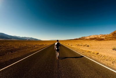 Rear view of man walking on road against sky