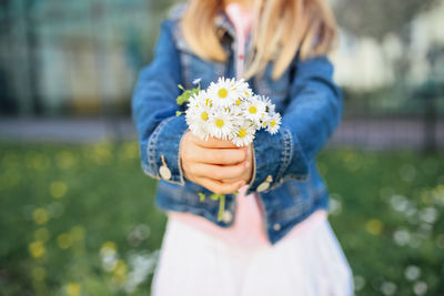 Midsection of girl holding flowers while standing on field