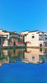 Reflection of buildings in water against clear blue sky