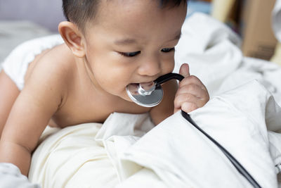 Cute baby boy biting stethoscope while lying on bed at home