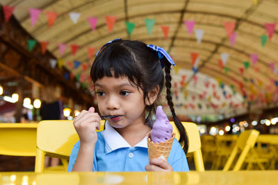 Cute girl eating ice cream while sitting on chair at restaurant