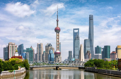 Modern buildings by river against cloudy sky in city