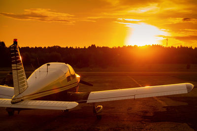 Airplane on runway against sky during sunset