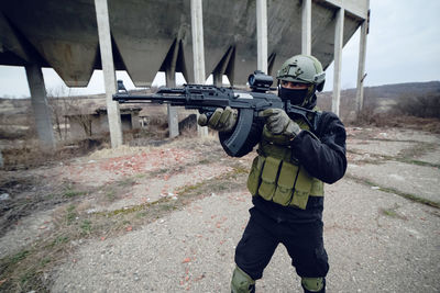 Army soldier aiming while standing against built structure