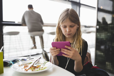 Woman looking through mobile phone while sitting on table