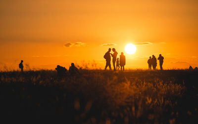 Silhouette people on field against orange sky