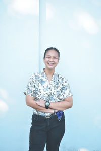 Portrait of smiling young woman standing against wall