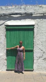 Full length portrait of young woman standing by wooden door