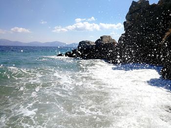 Sea waves splashing on shore against sky