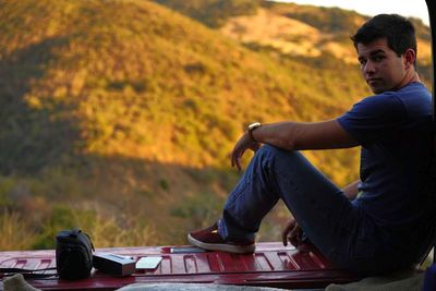 Full length portrait of young man sitting in pick-up truck against mountain