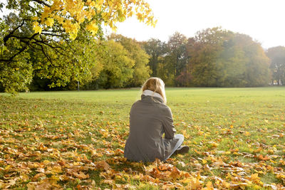 Rear view of woman sitting on field at park