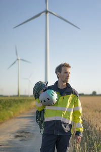 Technician standing on field path at a wind farm with climbing equipment