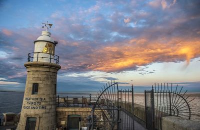 Lighthouse by sea against sky during sunset