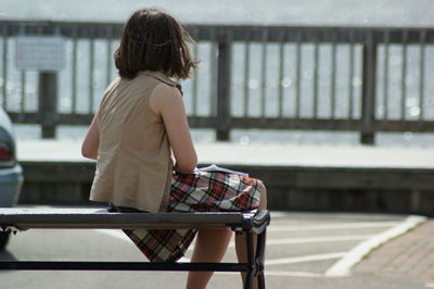 Rear view of woman sitting on bench on pier