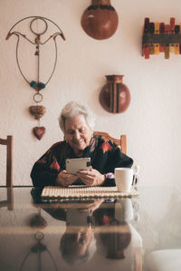 Smiling elderly female wearing warm clothes sitting at table with tablet and cup of tea looking at screen