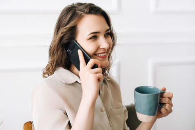 Happy young woman enjoying a phone call while savoring a drink in leisure time. joyful young woman