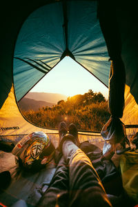 Low section of man relaxing at tent against sky during sunset