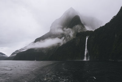 Scenic view of mitre peak, tour boat & waterfall at milford sound, nz