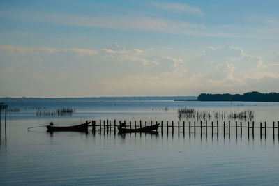 Wooden posts in sea against sky during sunset