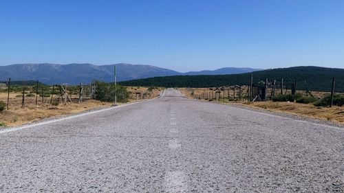 Empty road along landscape against clear blue sky