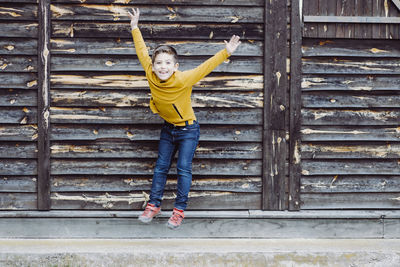 Full length portrait of boy jumping against wooden wall