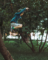 Side view of playful boy jumping on land against trees