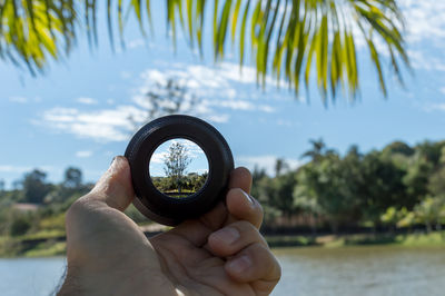 Close-up of hand holding lens against trees