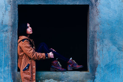 Side view of thoughtful young woman sitting on weathered window