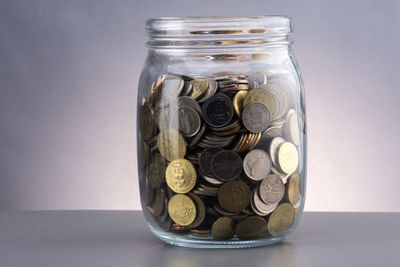 Close-up of coins in jar on table against white background