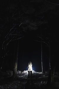 Spooky female ghost standing amidst trees in forest at night