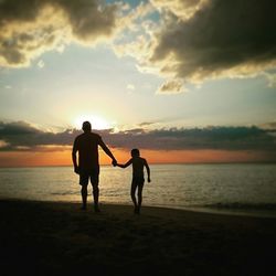 Silhouette man and kid holding hands on beach
