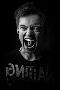 Portrait of young man shouting against black background