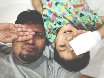 Father and son covering eyes while lying down on bed at home