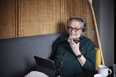 Senior man with headphones using phone and tablet in cafe