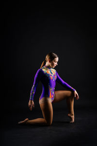 Young woman exercising against black background