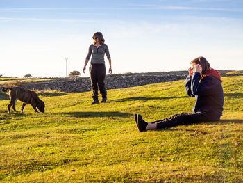 Girl and woman with dog on grass against sky