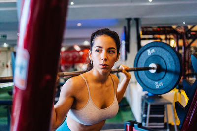 Side view portrait of young woman exercising in gym lifting 