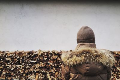 Rear view of person in fur jacket in front of stacked firewood
