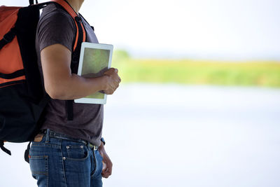 Man holding mobile phone while standing on field against sky