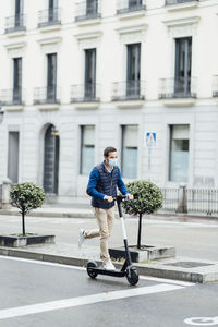 Young man riding electric push scooter on street in city during covid-19