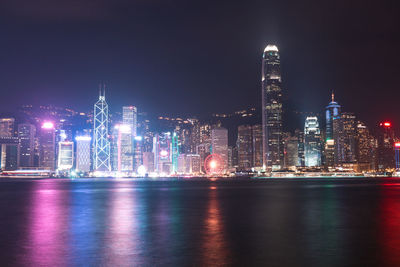 Illuminated city by river against sky at night