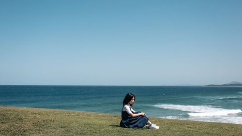Woman sitting at beach against clear sky