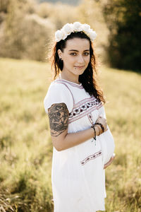 Portrait of smiling pregnant woman standing on grassy field